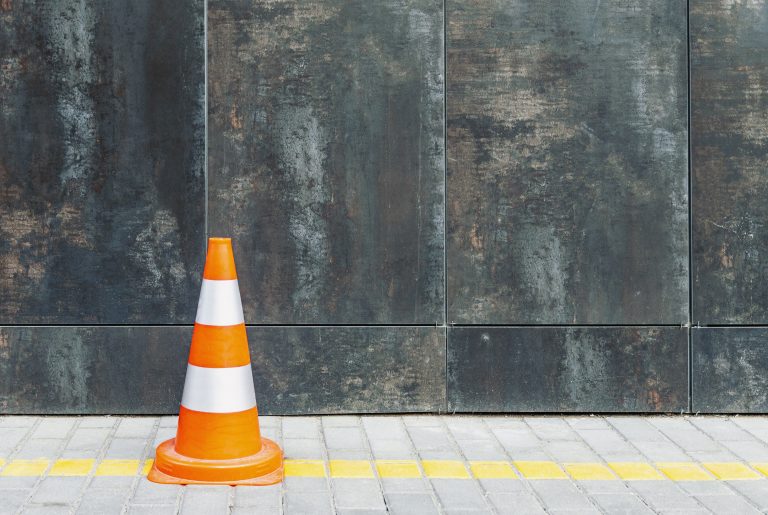 Plastic traffic cone against grunge wall with copy space, road cone and bollard standing on pavement